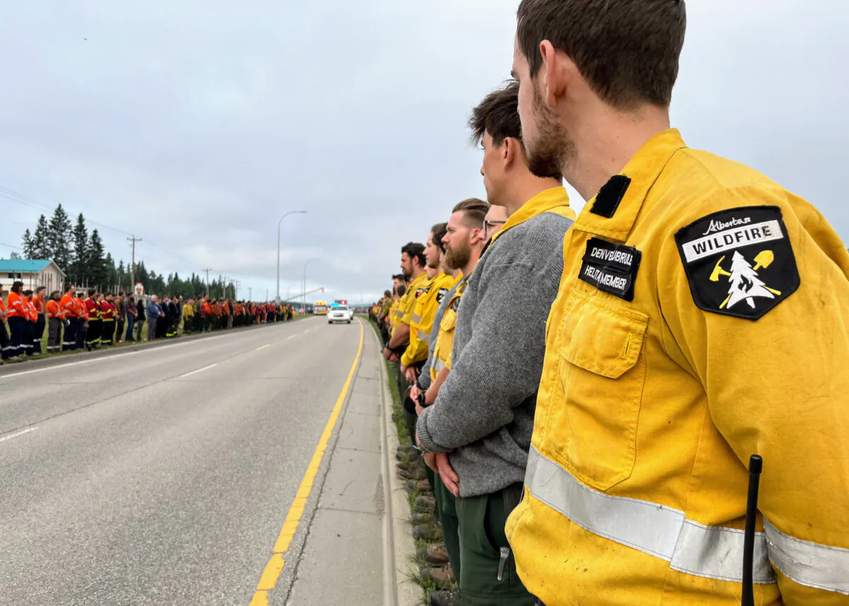 Comrades of a firefighter from Calgary who died while on duty in Jasper National Park stood on the sides of a roadway as a procession mourning his loss made its way past in Hinton, Alberta, east of Japer National Park, on Aug. 4, 2024. (The Canadian Press/HO-Alberta Wildfire)