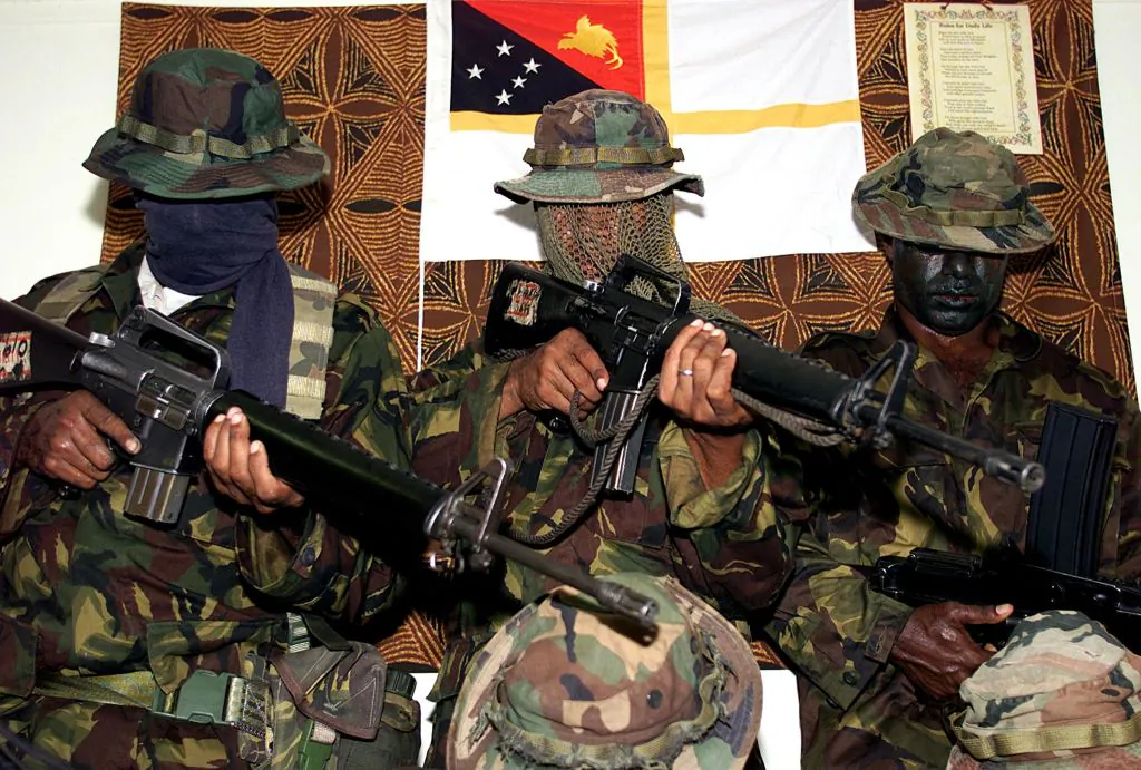 Rebel Papua New Guinea Defense Force soldiers, with faces obscured, display an array of weapons taken from the armoury at Murray Barracks in Port Moresby, March 23, 2001. (TORSTEN BLACKWOOD/AFP via Getty Images)