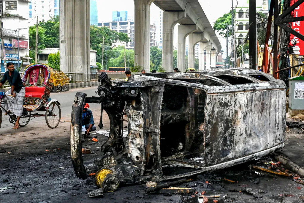 Passersby look at a burnt vehicle along a street amid anti-government protests in Dhaka, Bangladesh, on Aug. 5, 2024. (MUNIR UZ ZAMAN/AFP via Getty Images)