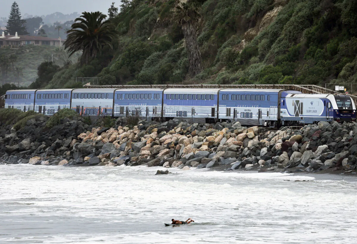 An Amtrak Pacific Surfliner train passes near a surfer during a sand replenishment project nearby along eroding shoreline on May 21, 2024 in San Clemente, California. (Mario Tama/Getty Images)