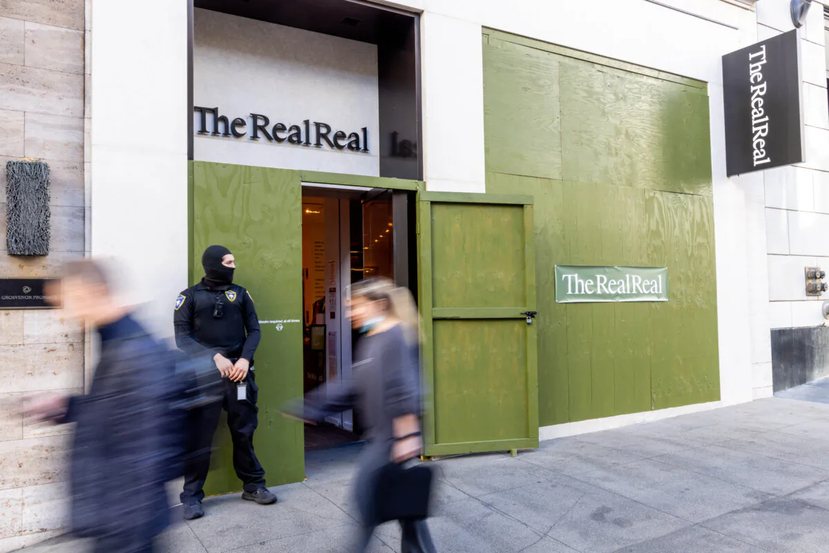 A security guard watches as pedestrians walk past The Real Real store, which has had its windows boarded, near Union Square in San Francisco on Nov. 30, 2021. (Ethan Swope/Getty Images)