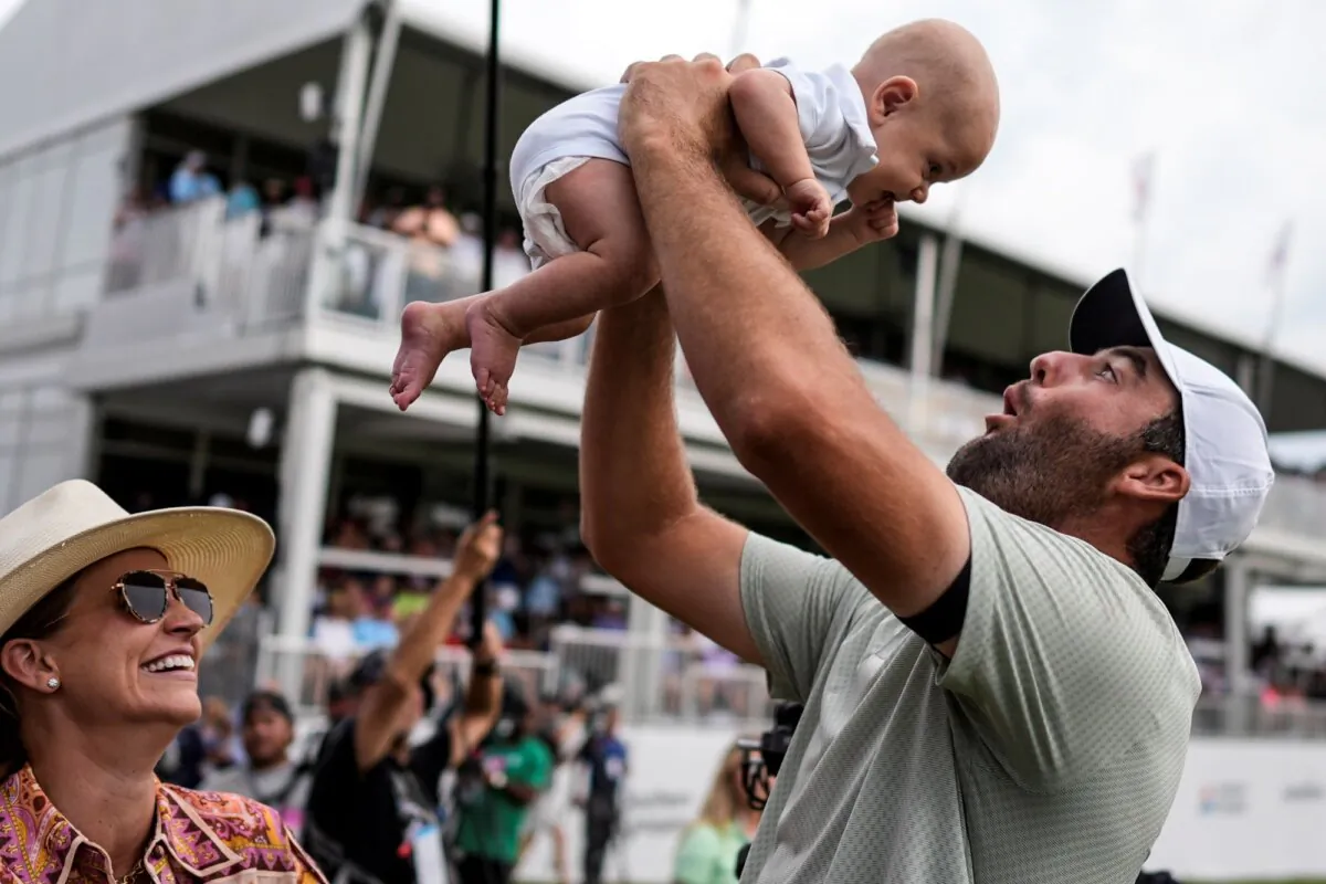 Scottie Scheffler holds his son, Bennett Ezra Scheffler, as his wife, Meredith Scudder, watches on the 18th green after Scheffler won the Tour Championship in Atlanta on Sept. 1, 2024. (Mike Stewart/AP Photo)
