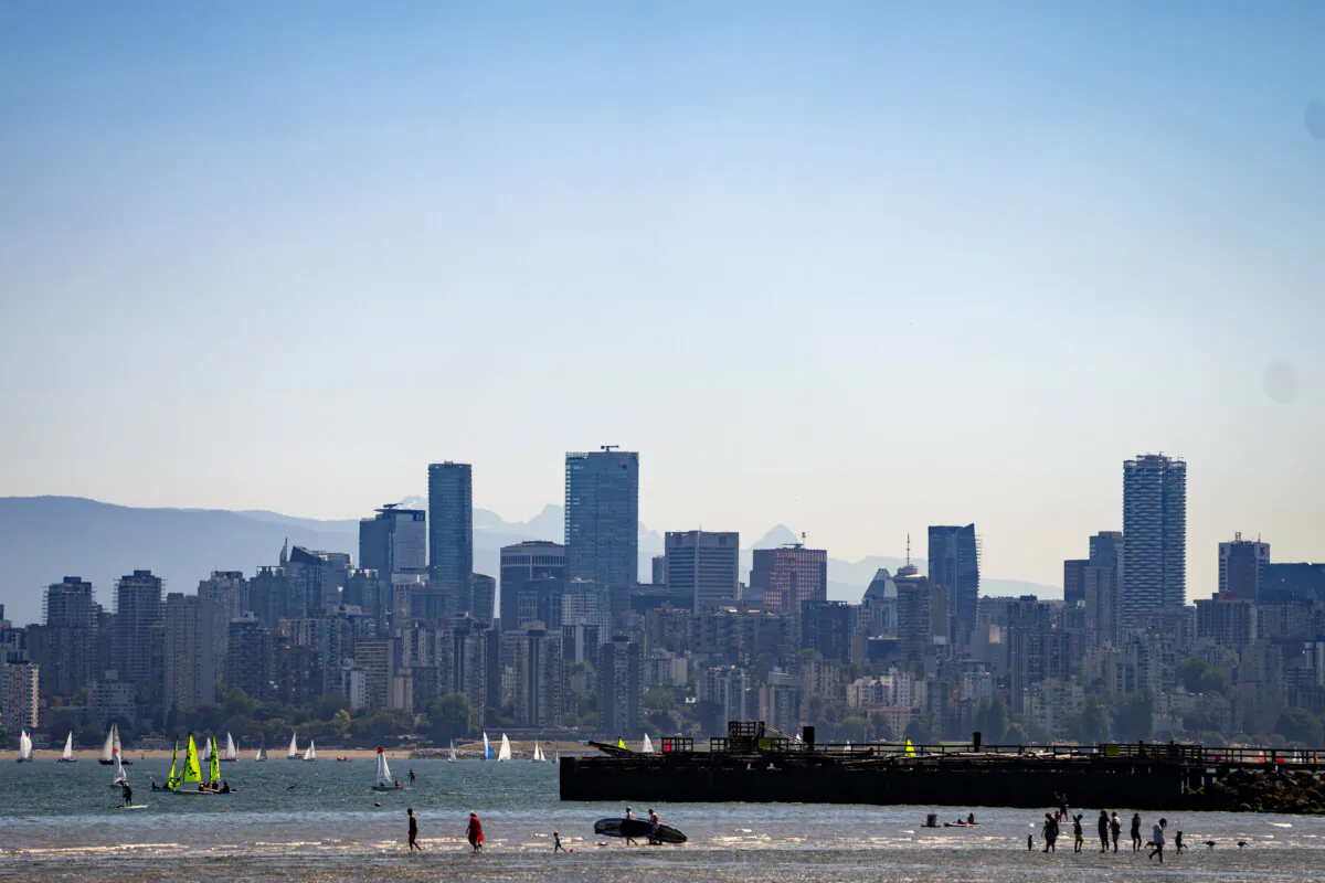 People enjoy the beach during low tide as the city skyline looms in the background, in Vancouver, on July 7, 2024. (The Canadian Press/Ethan Cairns)