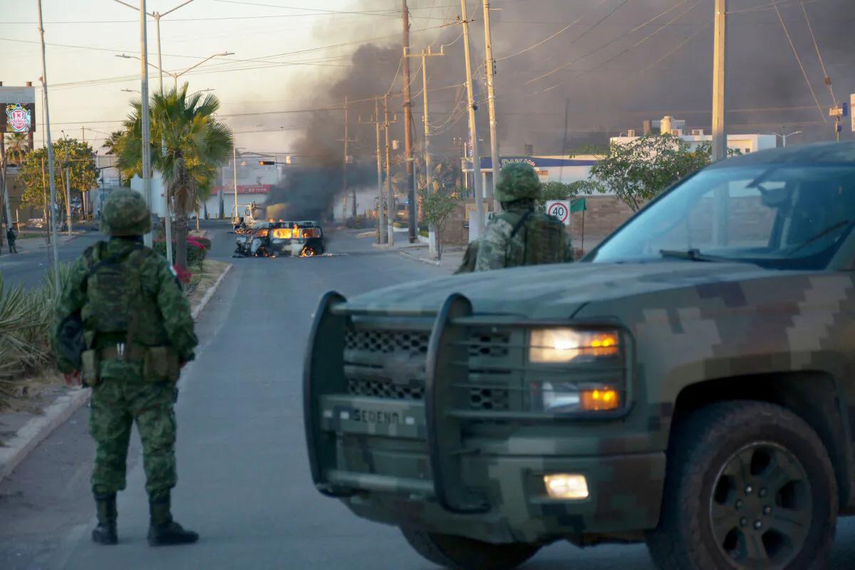 Mexican soldiers stand guard near burning vehicles on a street during an operation to arrest Ovidio Guzman, accused of leading a faction of the notorious Sinaloa cartel, in Culiacan, Sinaloa state, Mexico, on Jan. 5, 2023. (Juan Carlos Cruz/AFP via Getty Images)