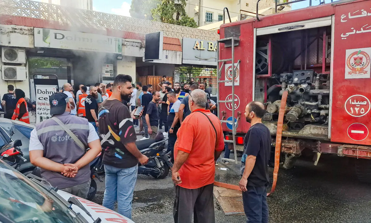 People gather as smoke rises from a mobile shop in Sidon, Lebanon, on Sept. 18, 2024. (Hassan Hankir/Reuters)
