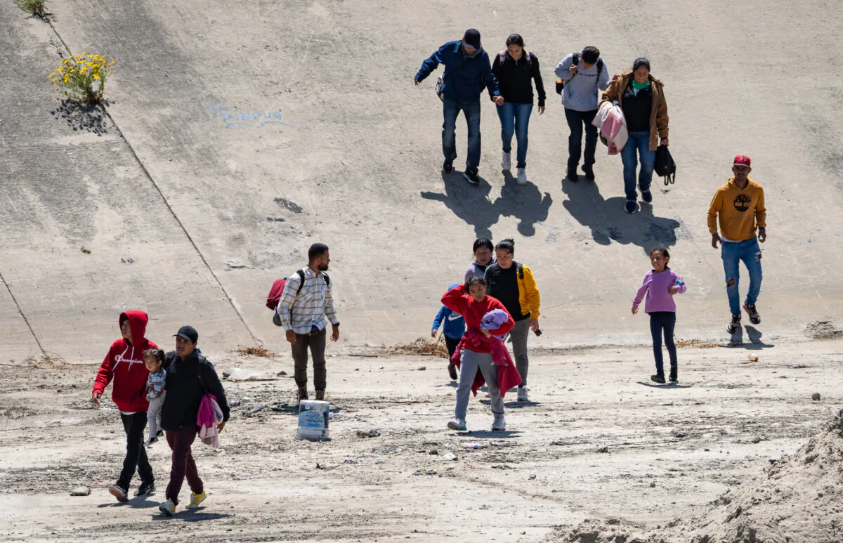 People cross the Tijuana River and move toward the US border wall in Tijuana, Mexico, on May 11, 2023. (John Fredricks/The Epoch Times)
