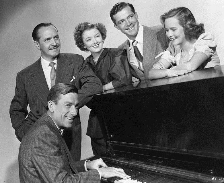 (L-R) Hoagy Carmichael plays the piano in a publicity shot for "The Best Years of Our Lives," with Frederick March, Myrna Loy, Dana Andrews, and Theresa Wright. (Public Domain)