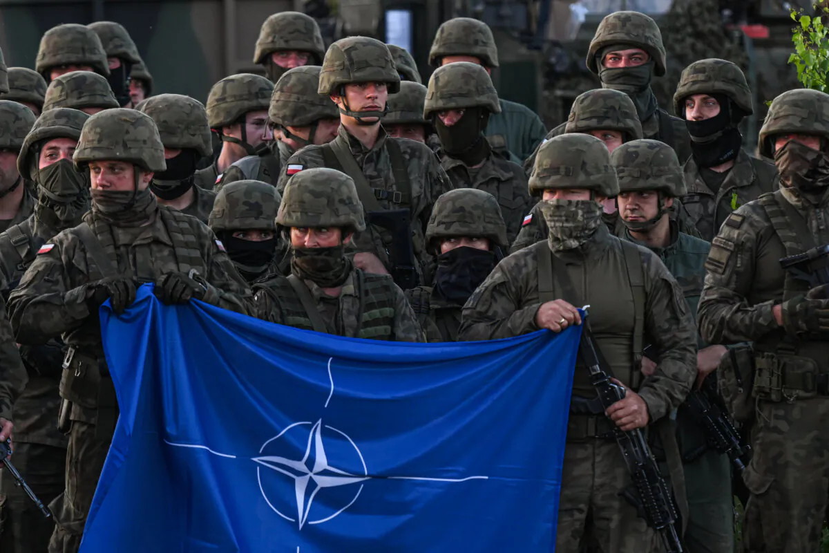 Polish soldiers hold a NATO flag during a group photo after a training demonstration with the NATO multinational Enhanced Forward Presence battle group at the Orzysz training ground in Orzysz, Poland, on July 3, 2022. (Omar Marques/Getty Images)
