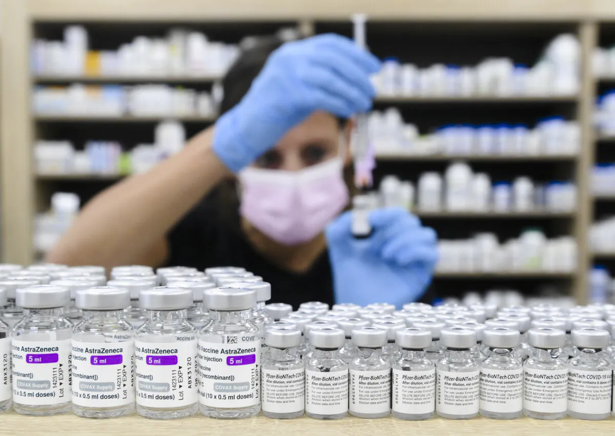 A pharmacist prepares a dose behind a counter lined with vials of COVID-19 vaccines in Toronto on June 18, 2021. (Nathan Denette/The Canadian Press)