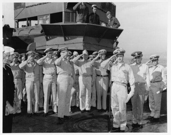 Officers salute as the United States national anthem is played during recommissioning ceremonies on her foredeck, while she was moored in Hiro Wan, Japan on 29 October 1945. Her new commanding officer, Lieutenant Commander Harold H. Ellison, is standing by the microphone in the right-center foreground. (Official U.S. Navy Photograph, now in the collections of the National Archives.)