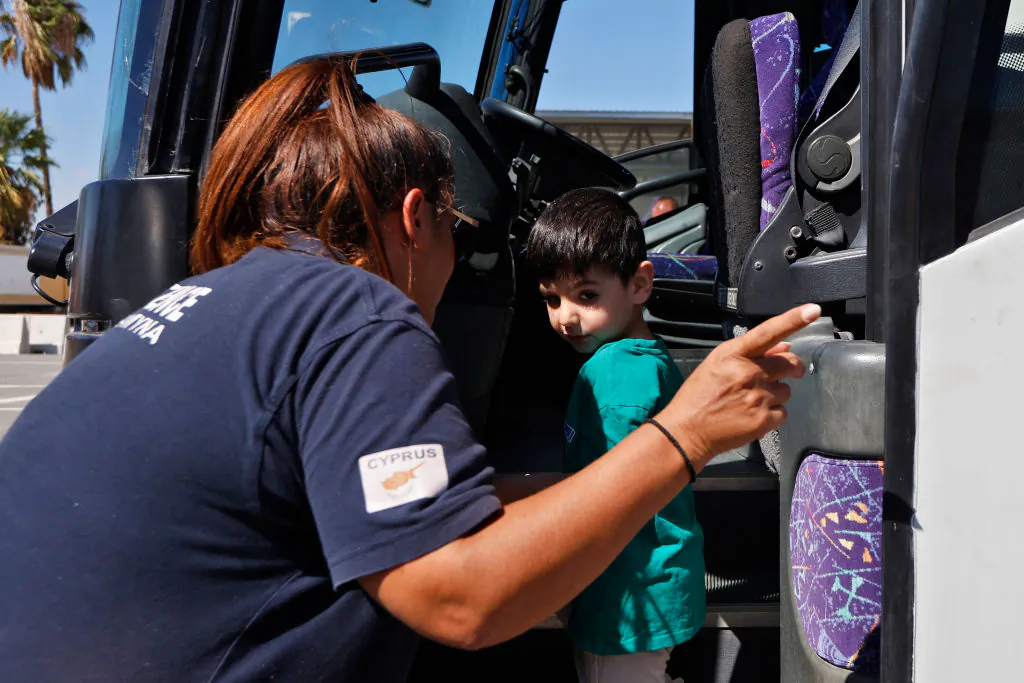 LARNACA, CYPRUS - OCTOBER 5: A Cypriot Civil Defence volunteer helps a child board a bus as Australians nationals arrive at Larnaca International Airport from Beirut on October 5, 2024 in Larnaca, Cyprus. As Israel's war with Hezbollah has led to escalating violence across Lebanon, the Mediterranean island of Cyprus is becoming a central waypoint for foreign nationals evacuating from Lebanon. During the 2006 Lebanon war, foreign governments evacuated many of their citizens by naval vessel to Cyprus. (Photo by Alexis Mitas/Getty Images)