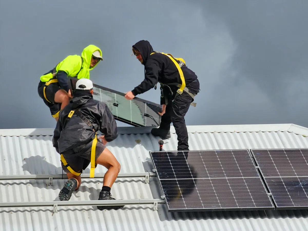 Three men install solar panels on a roof as storm clouds approach in Albany, Western Australia, on Aug. 29, 2024. (Susan Mortimer/The Epoch Times)