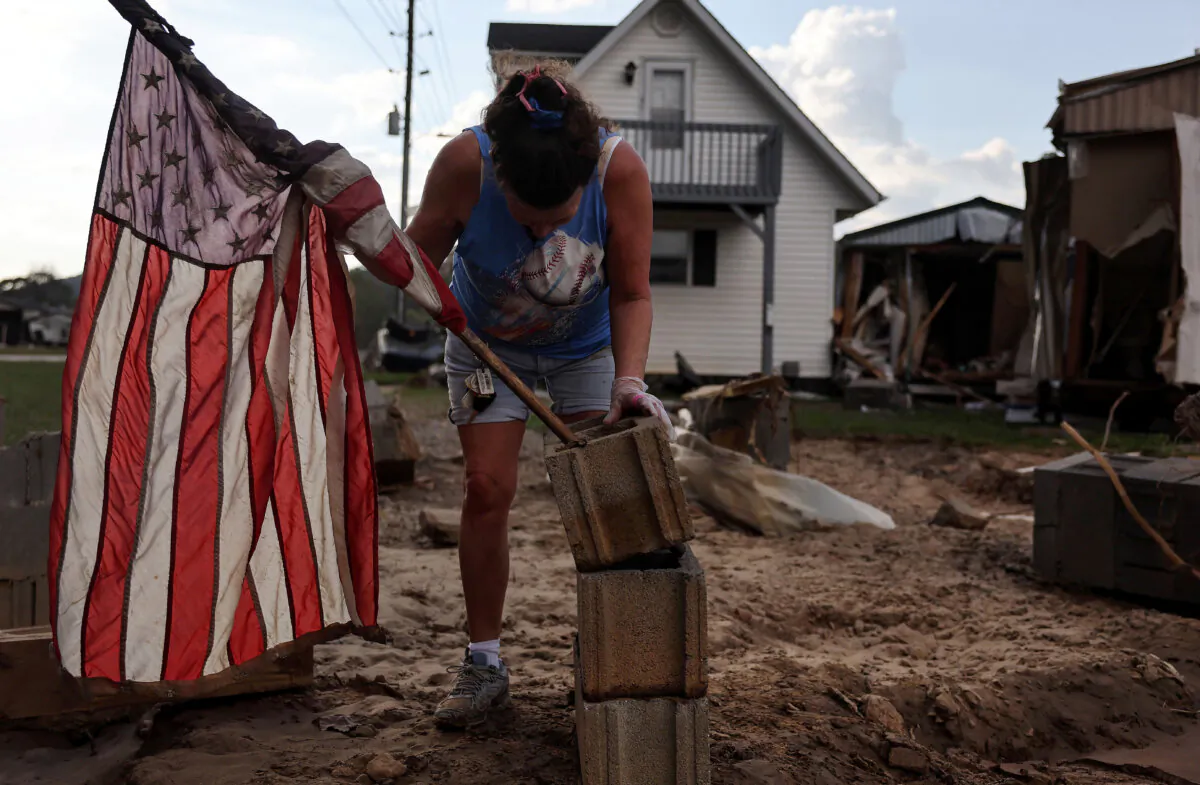 Roxanne Brooks mounts an American flag to a stack of cinderblocks outside her friend's destroyed mobile home (R) in the aftermath of Hurricane Helene flooding in Swannanoa, N.C., on Oct. 6, 2024. (Mario Tama/Getty Images)