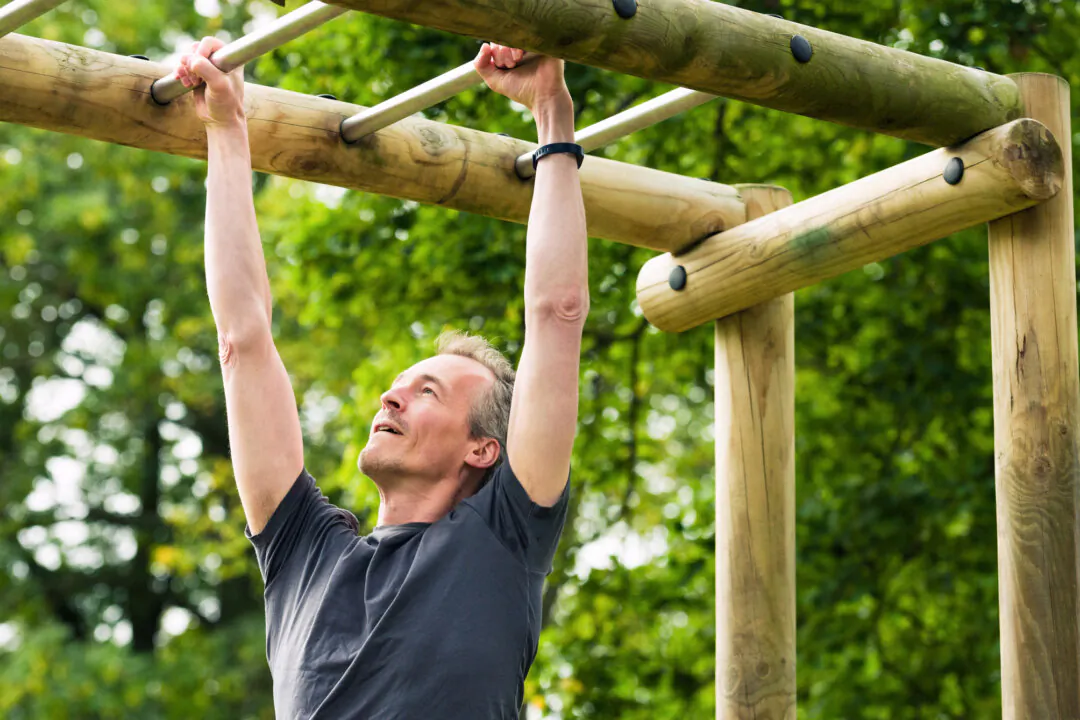 A man training on an outdoor assault course, concentrating as he moves along raised monkey bars.