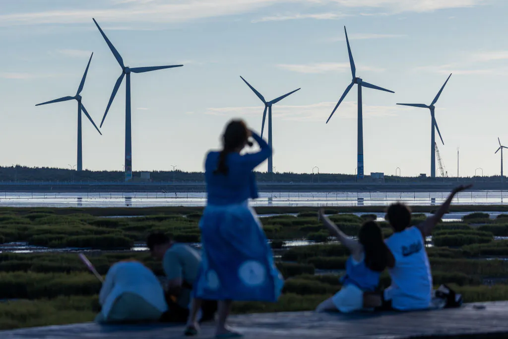 Wind turbines stand behind visitors at Gaomei wetland during sunset in Taichung, Taiwan on Aug. 22, 2024. (Annabelle Chih/Getty Images)