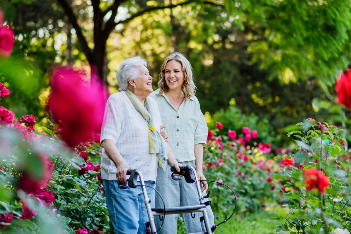 Adult granddaguhter supporting her senior grandmother when taking her for walk with walker in park in summer. (Shutterstock)