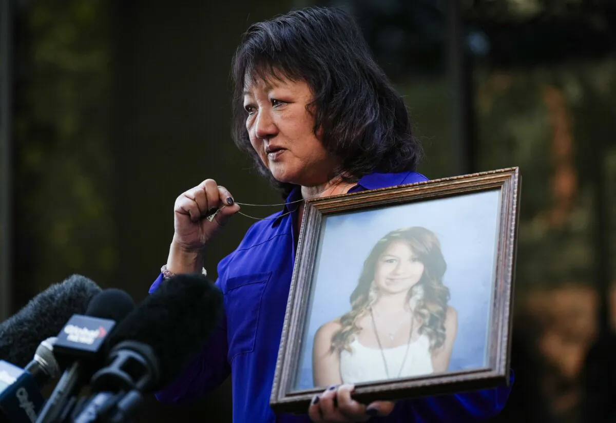 Carol Todd holds a photo of her late teenage daughter Amanda Todd, who died by suicide in 2012, and the necklace she was wearing in the school photo as she speaks outside B.C. Supreme Court in New Westminster, B.C., on Oct. 14, 2022. (The Canadian Press/Darryl Dyck)
