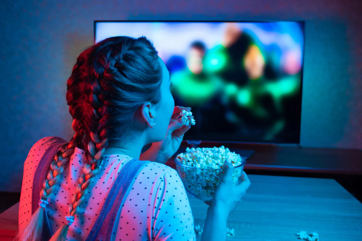 A young girl watches movies and eats popcorn in a stock photo. (Anton27/Shutterstock)
