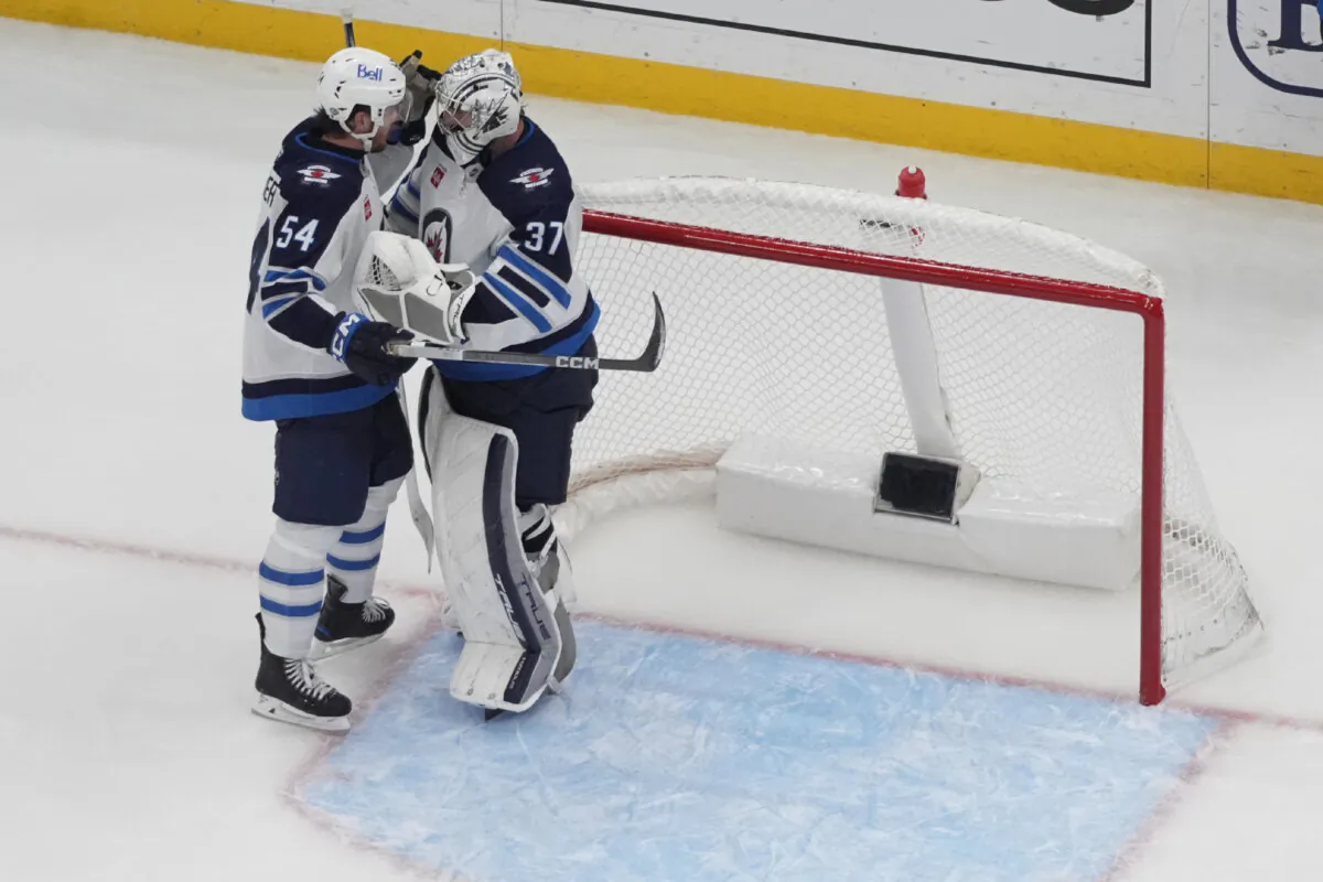 Winnipeg Jets goaltender Connor Hellebuyck (37) and teammate Dylan Samberg (54) celebrate a 3-2 victory over the St. Louis Blues in an NHL hockey game in St. Louis, on Oct. 22, 2024. (Jeff Roberson/AP Photo)