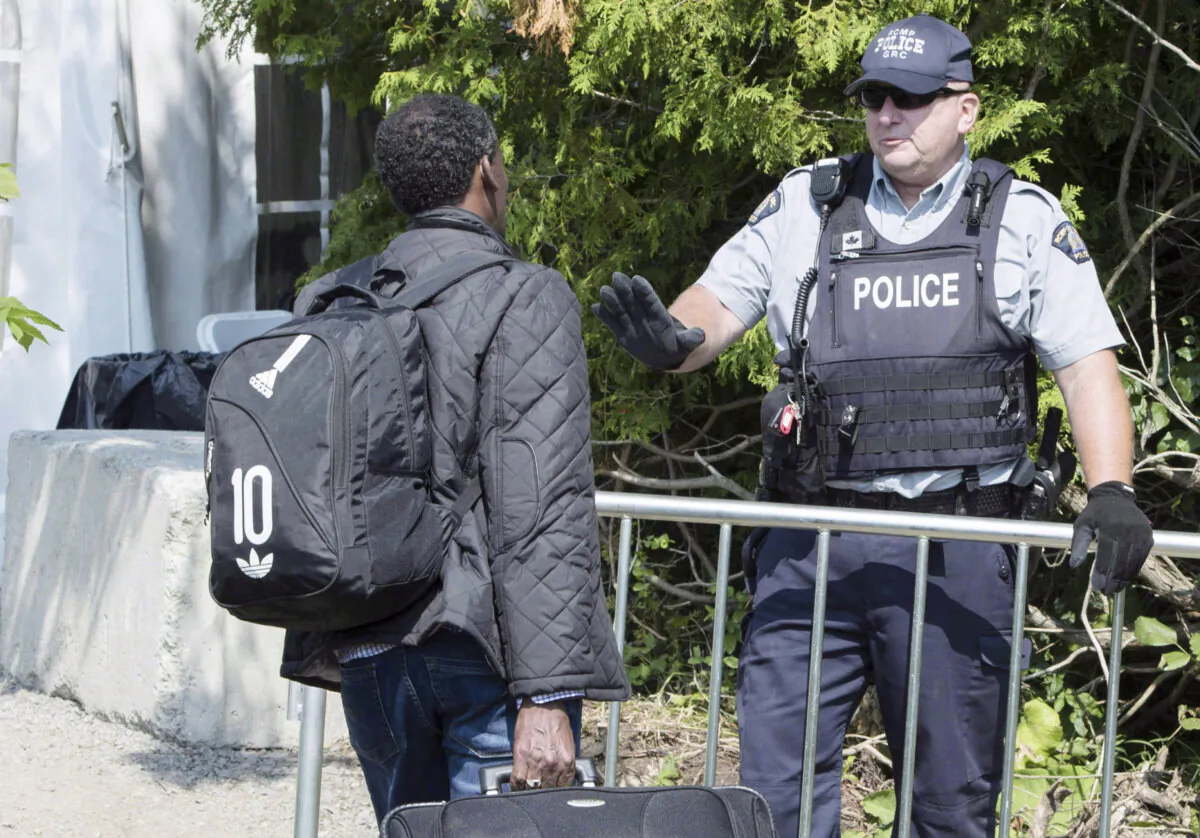 An asylum seeker is questioned by an RCMP officer as he crosses the border into Canada from the United States near Champlain, New York, on Aug. 21, 2017. (The Canadian Press/Paul Chiasson)
