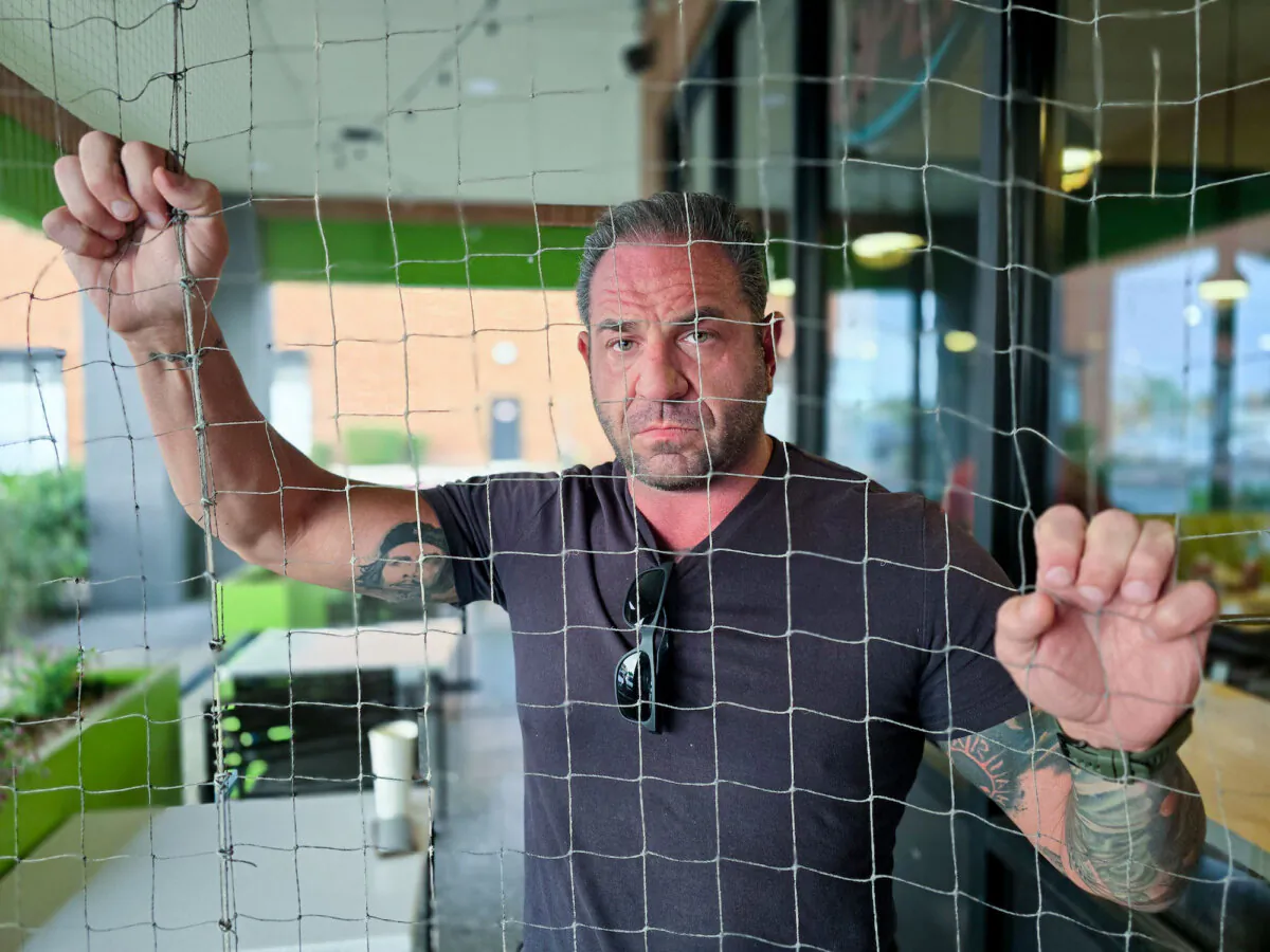 Lysander Caligo, a former U.S. Marine who served in Afghanistan, stands behind a mesh barrier at a restaurant in Mesa, Ariz., on Nov. 3, 2024. (Allan Stein/The Epoch Times)