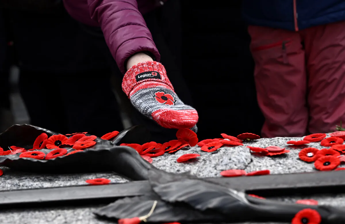 A person wearing a mitten embroidered with a poppy lays a poppy on the Tomb of the Unknown Soldier, after the National Remembrance Day Ceremony at the National War Memorial in Ottawa, on Nov. 11, 2023. (The Canadian Press/Justin Tang)