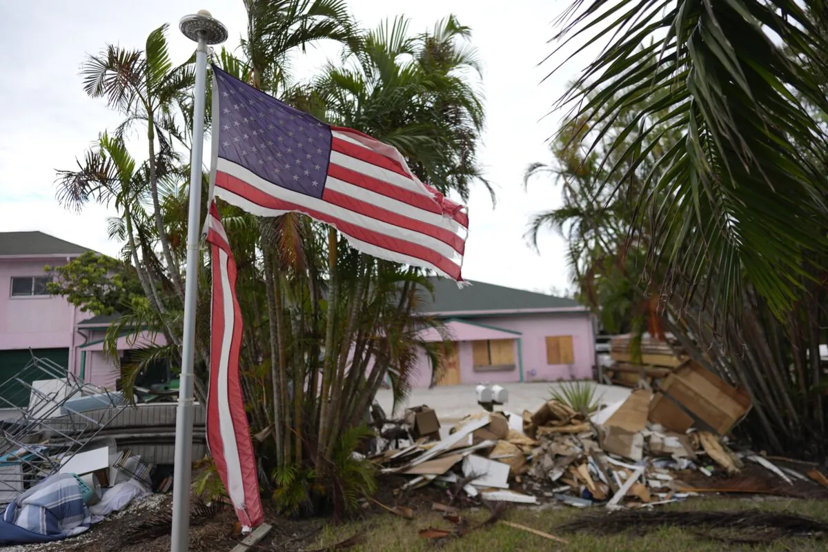 A tattered American flag flaps outside a home with furniture and household items damaged by Hurricane Helene piled outside along the street awaiting pickup ahead of the arrival of Hurricane Milton in Holmes Beach on Anna Maria Island, Fla., on Oct. 8, 2024. (Rebecca Blackwell/AP Photo)