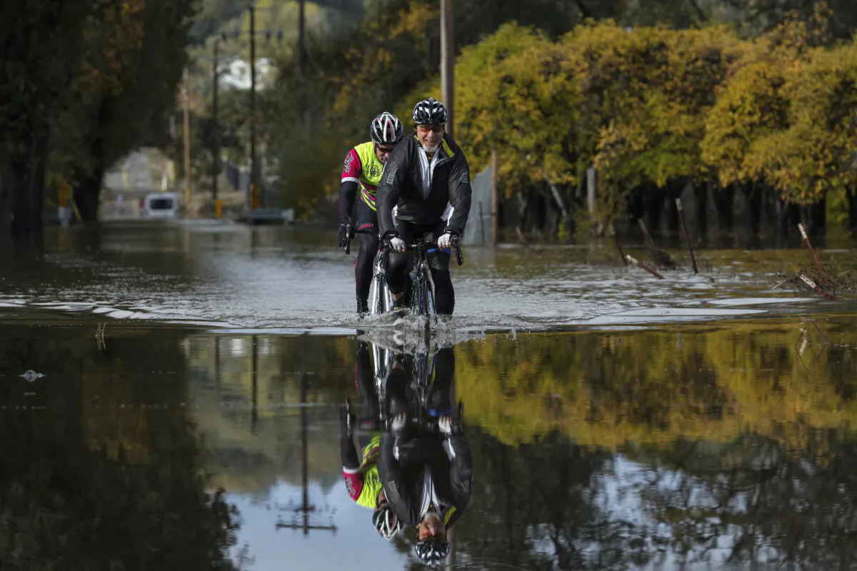 Dave Edmonds (R) and Mike Raasch ride their bicycles on a flooded road in Windsor, Calif., on Nov. 23, 2024. (Godofredo A. Vásquez/AP Photo)