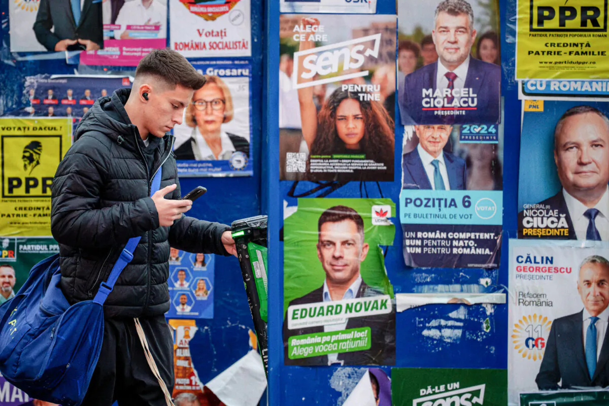 A young man on his cellphone walks past election posters from the main presidential  candidates, in Bucharest, Romania, on Nov. 22, 2024. (Andreea Alexandru/AP)