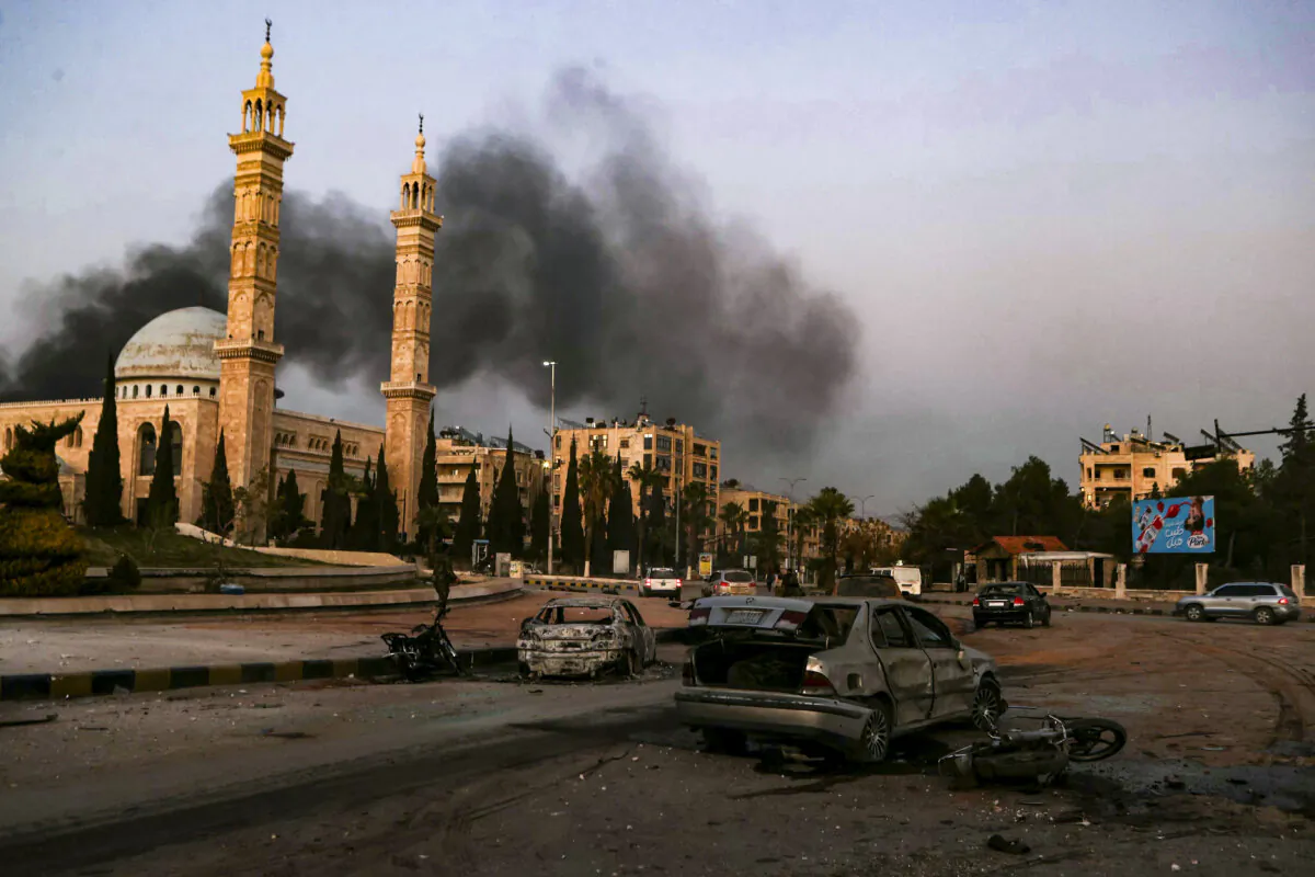 Smoke billows in the distance as damaged cars are seen at the site of Syrian regime airstrikes targeting anti-regime fighters in Aleppo, in Syria's northwestern Idlib province, on Nov. 30, 2024. (Aaref Watad/AFP via Getty Images)