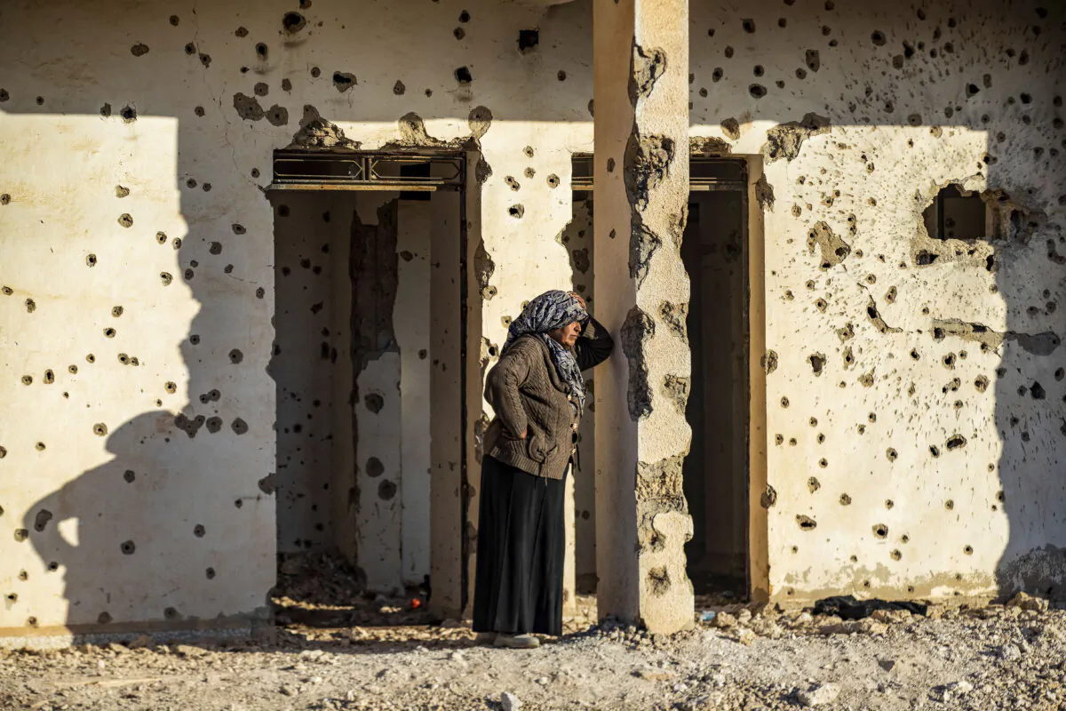 A Syrian Kurdish woman, fleeing from north of Aleppo, stands leaning on a bullet-riddled wall upon arriving in Tabqa, on the western outskirts of Raqa, on Dec. 4, 2024. (Delil SOULEIMAN/AFP via Getty Images)