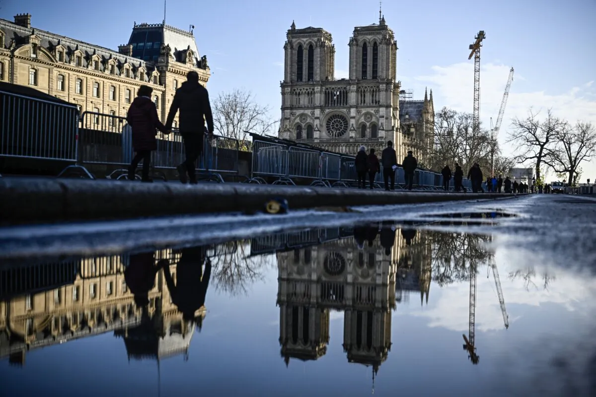 Pedestrians pass by the security barriers and fences placed around the Notre-Dame de Paris cathedral on the eve ahead of its official reopening after more than five-year of reconstruction work following the April 15, 2019 fire, in Paris, on Dec. 6, 2024. (Julien de Rosa/AFP via Getty Images)
