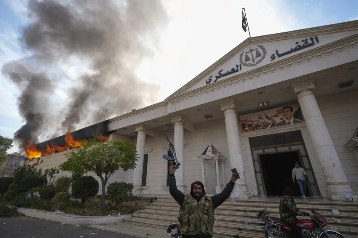 Opposition fighters celebrate as they burn down a military court in Damascus, Syria, on Dec. 8, 2024. (The Canadian Press/AP/Hussein Malla)