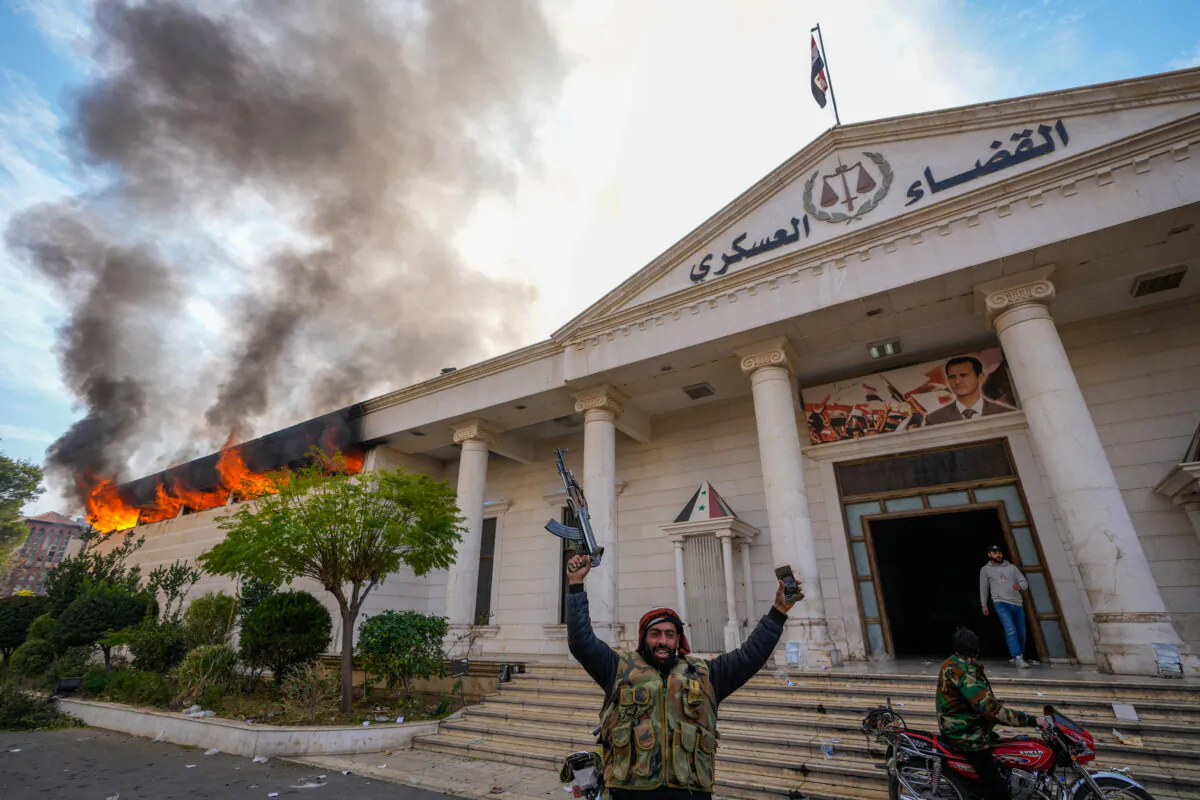 Opposition fighters celebrate as they burn down a military court in Damascus, Syria, on Dec. 8, 2024. (The Canadian Press/AP-Hussein Malla）