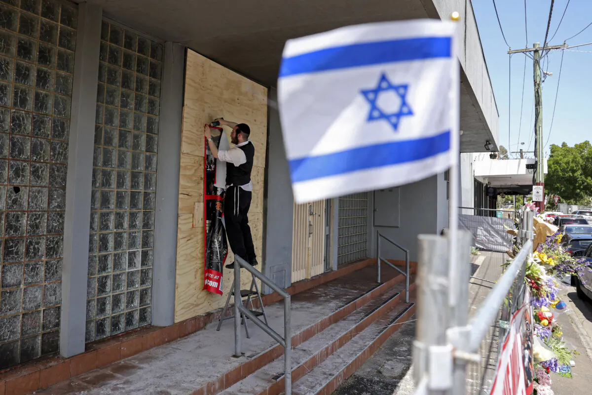 A member of the Jewish community staples a poster to the front of the damaged Adass Israel Synagogue in the Melbourne suburb of Ripponlea in Australia on Dec. 9, 2024. (Martin Keep/AFP via Getty Images)