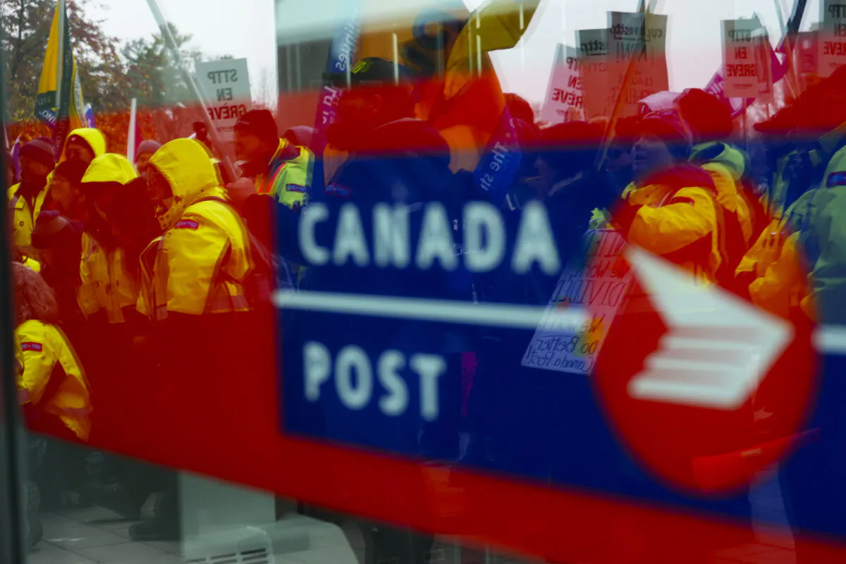 Canada Post employees and supporters rally as they are reflected in a window at Canada Post headquarters in Ottawa, on Nov. 28, 2024. (The Canadian Press/Sean Kilpatrick)