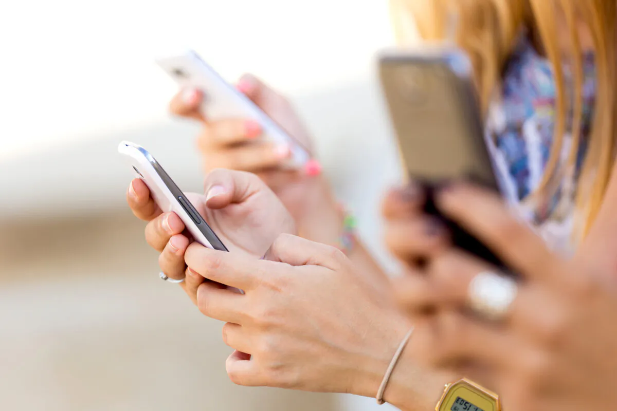 Three girls use their smartphones at a park in a stock photo. (Josep Suria/Shutterstock)