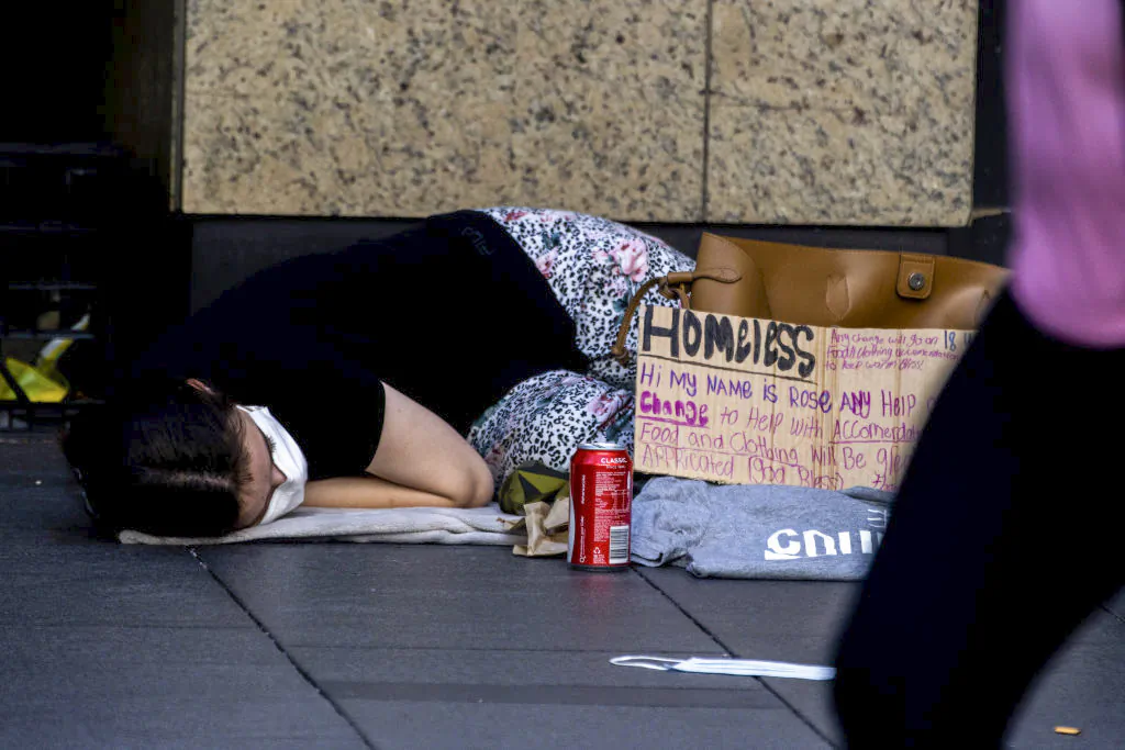 A homeless girl sleeps on the ground by a sign asking for food and clothing in Sydney, Australia, on Jan. 18, 2021. (Jenny Evans/Getty Images)