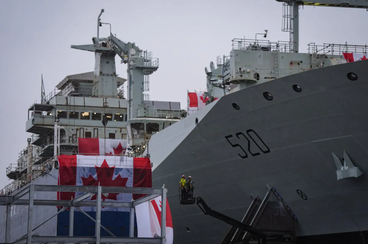 Workers are seen on a lift beside the new Royal Canadian Navy Joint Support vessel before a launch and naming ceremony at Seaspan Shipyards, in North Vancouver, B.C., on Dec. 13, 2024. (The Canadian Press/Darryl Dyck) 