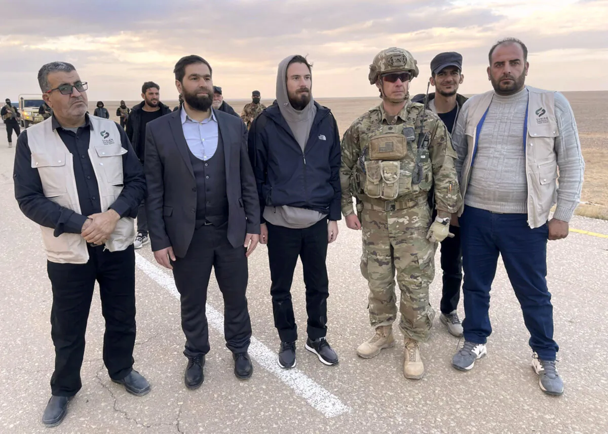 This image provided by Mouaz Moustafa shows Travis Timmerman, center, standing with a member of the U.S. military and representatives of Syria's transitional government and opposition activists near the Syria-Jordanian border on Dec. 13, 2024. (Mouaz Moustafa via AP)