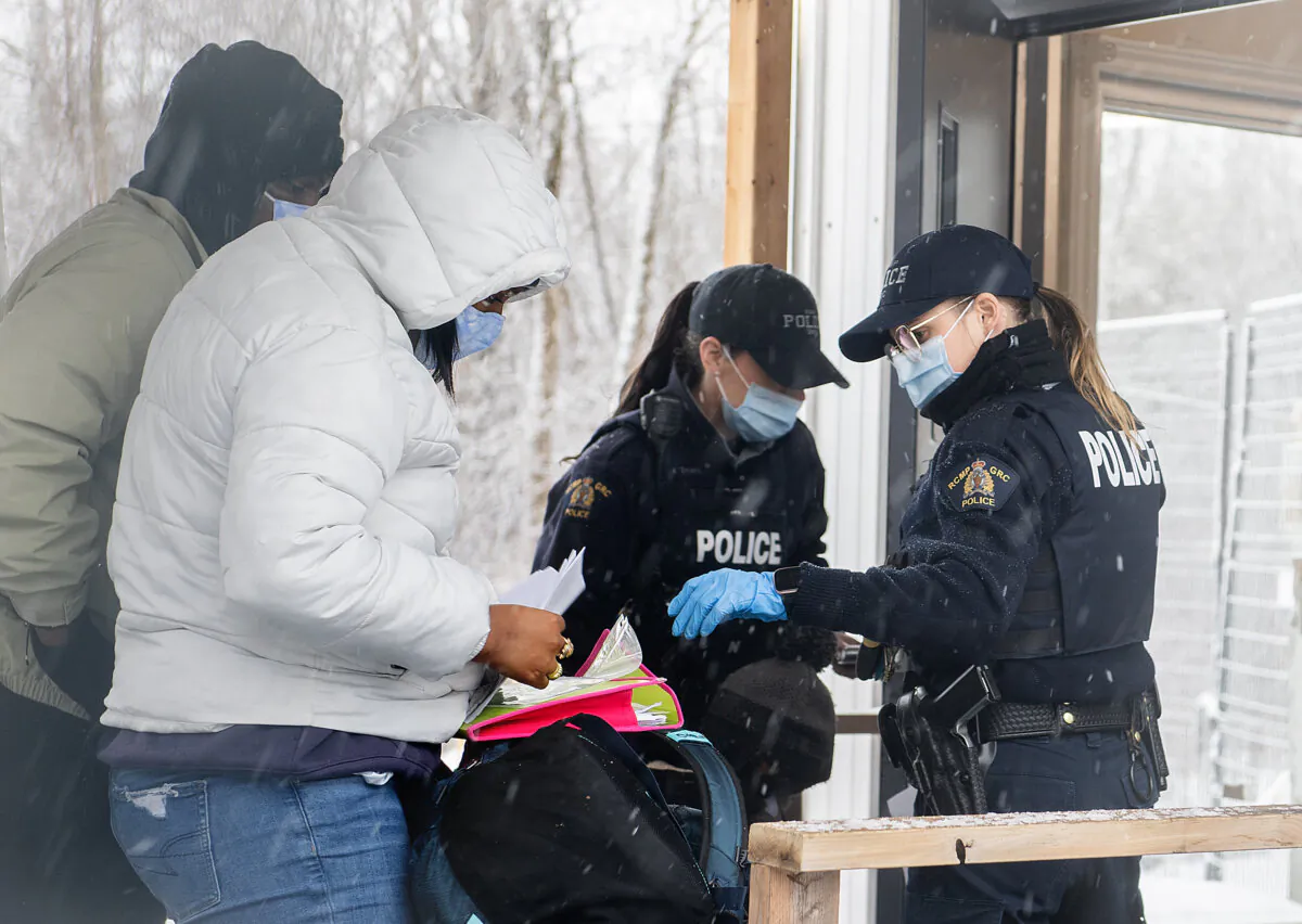 RCMP officers checks the credentials of two people who entered Canada via Roxham road on the Canada/US border in Hemmingford, Que., on March 25, 2023. (The Canadian Press/Graham Hughes) 