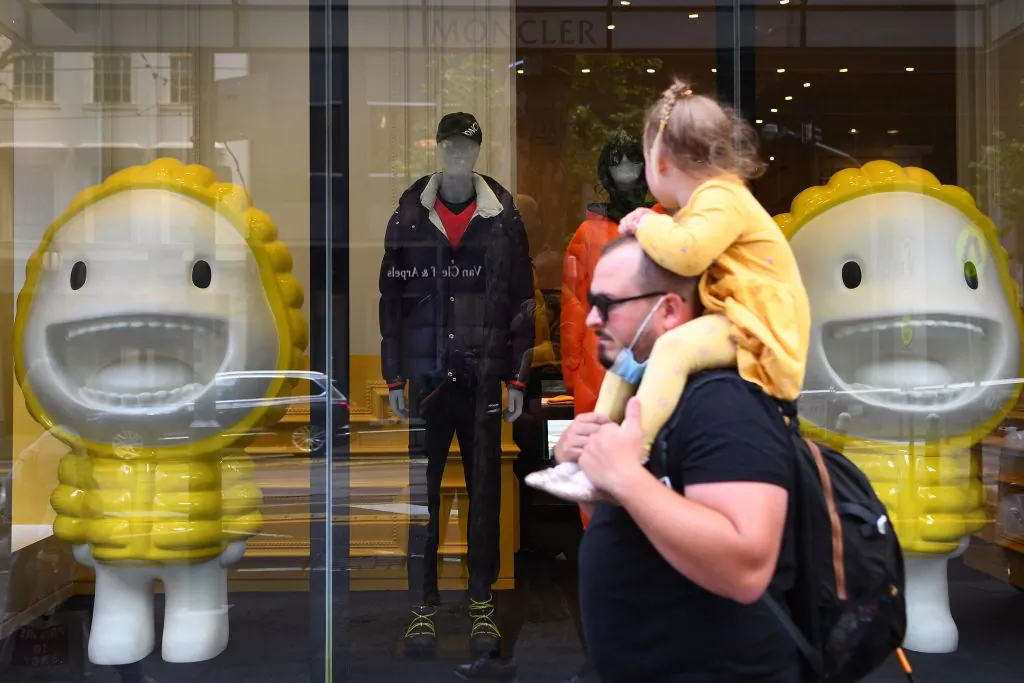 A father and daughter pass a store front in Melbourne, Australia, on Oct. 28, 2021. (WILLIAM WEST/AFP via Getty Images)