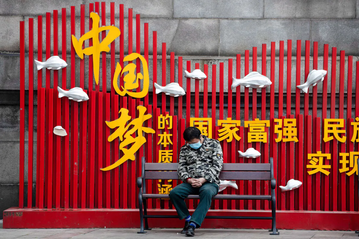A resident wearing a mask naps on a bench near the CCP's propaganda slogan "Chinese dream" in Wuhan, China, on April 1, 2020. (Ng Han Guan/AP Photo)