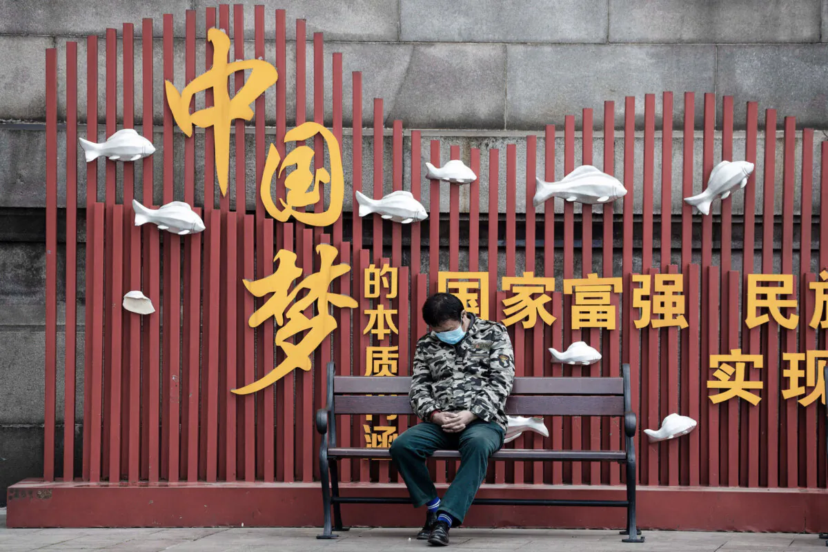 A resident wearing a mask naps on a bench near the Chinese Communist Party's propaganda slogan "Chinese dream" in Wuhan, China, on April 1, 2020. (Ng Han Guan/AP Photo)