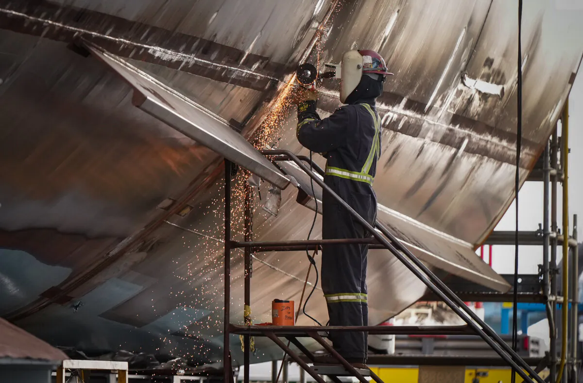 A worker uses an angle grinder on a vessel under construction at a shipyards, in North Vancouver, B.C., on Oct. 10, 2024. (The Canadian Press/Darryl Dyck) 
