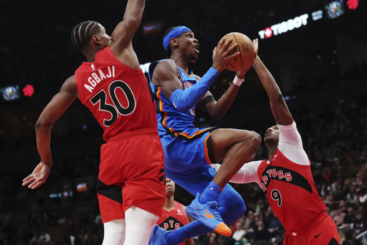 Oklahoma City Thunder's Shai Gilgeous-Alexander, center, drives between Toronto Raptors' Ochai Agbaji (30) and RJ Barrett (9) during second-half NBA basketball game action in Toronto, Thursday, Dec. 5, 2024. (Nathan Denette/The Canadian Press via AP)