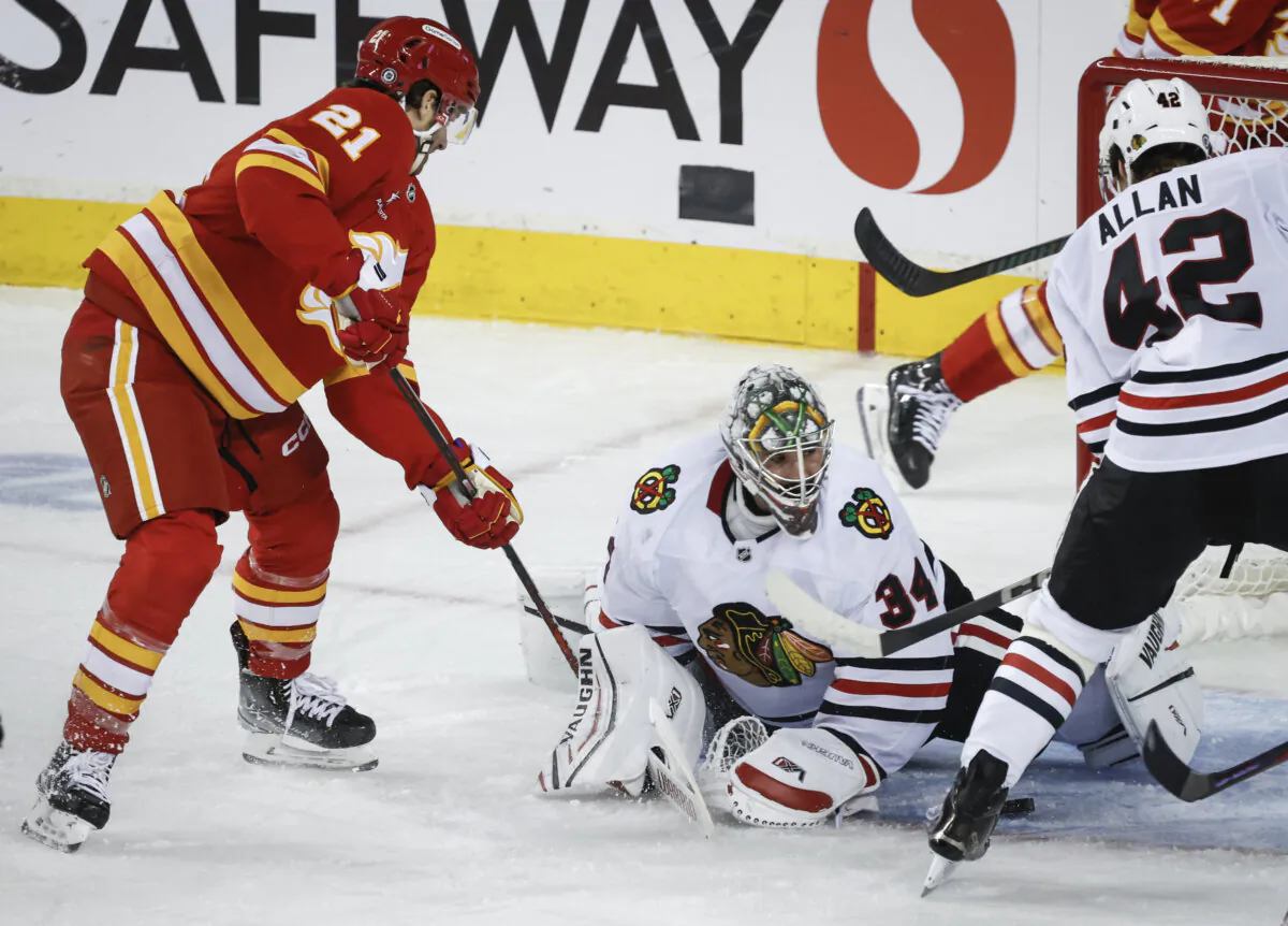 Chicago Blackhawks goalie Petr Mrazek, center, tries to grab the puck as Calgary Flames' Kevin Rooney (21) digs for it during the second period of an NHL hockey game in Calgary, Alberta, Saturday, Dec. 21, 2024. (Jeff McIntosh/The Canadian Press via AP)