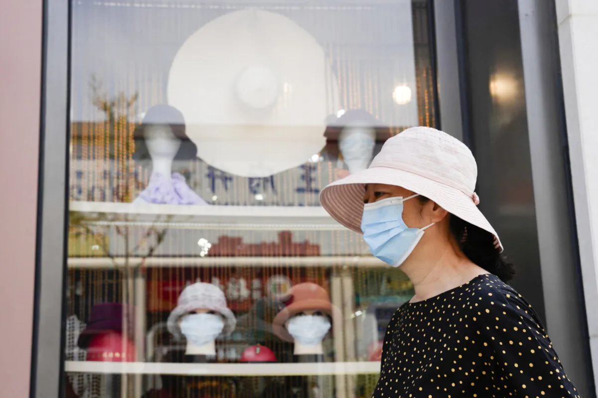A woman wearing mask passes by mannequin heads wearing masks in a hat shop in Beijing on Sept. 9, 2022. (Ng Han Guan/AP Photo)