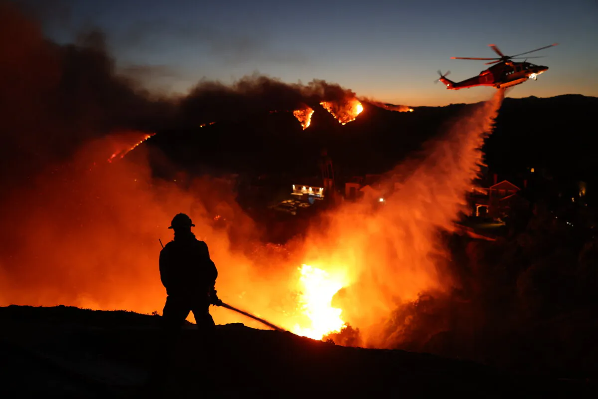 Fire personnel respond to homes destroyed while a helicopter drops water as the Palisades Fire grows in Pacific Palisades, Calif., on Jan. 7, 2025. (David Swanson/AFP via Getty Images)