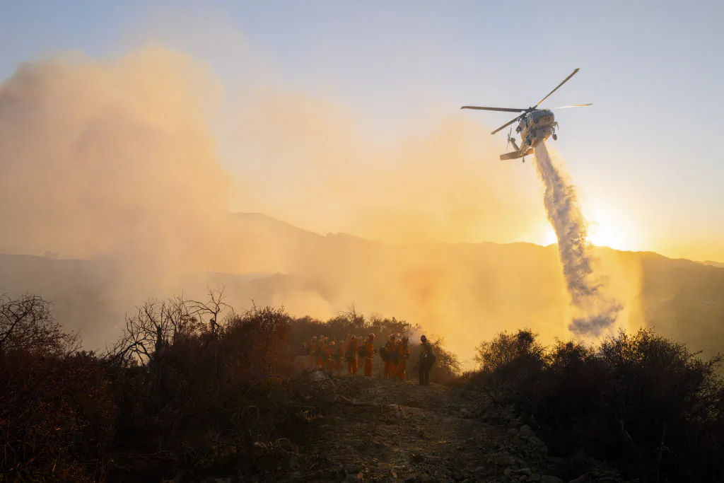 A firefighting helicopter drops water while smoke rises, in this file photo. (Ali Matin/Middle East Images/AFP via Getty Images)